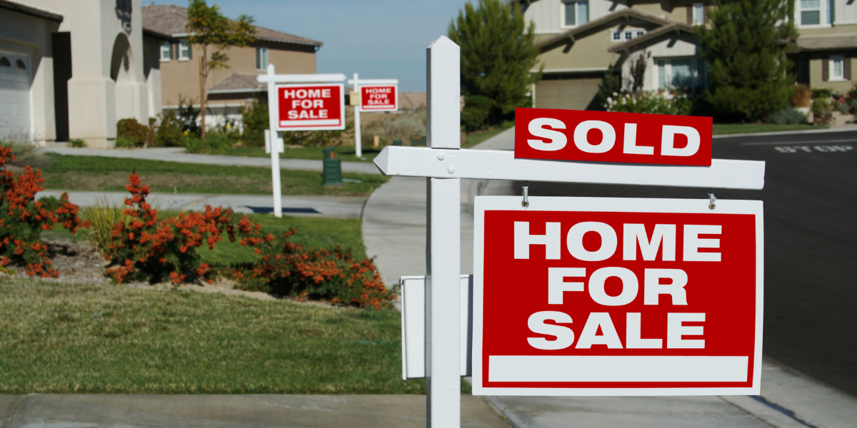 Suburban neighborhood with multiple 'Home for Sale' signs, one marked 'Sold' in the foreground.